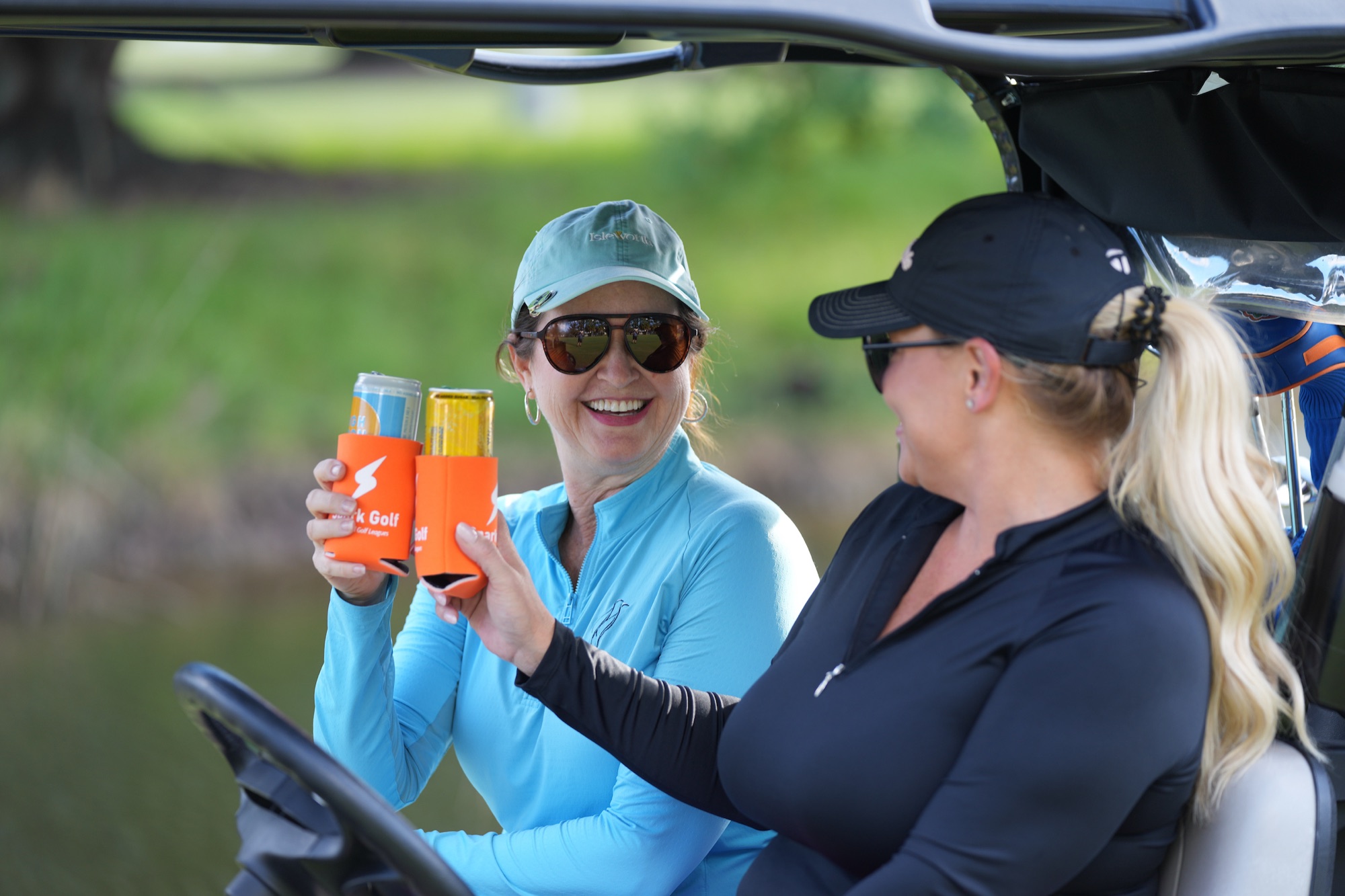 Two golfers toasting drinks in a golf cart