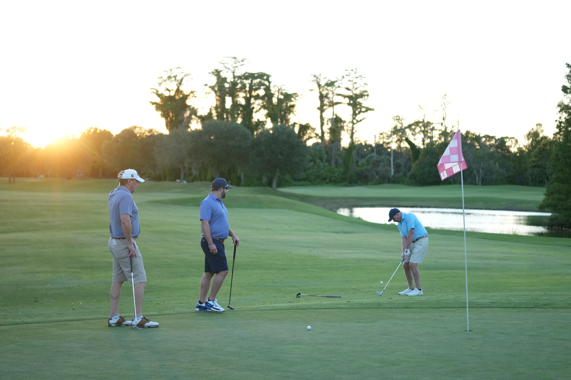 Golfers chipping onto the green at sunset